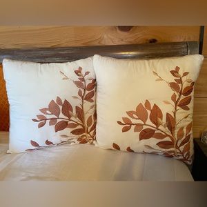 Pair of white 18” pillows with embroidered flowers and beige piping.